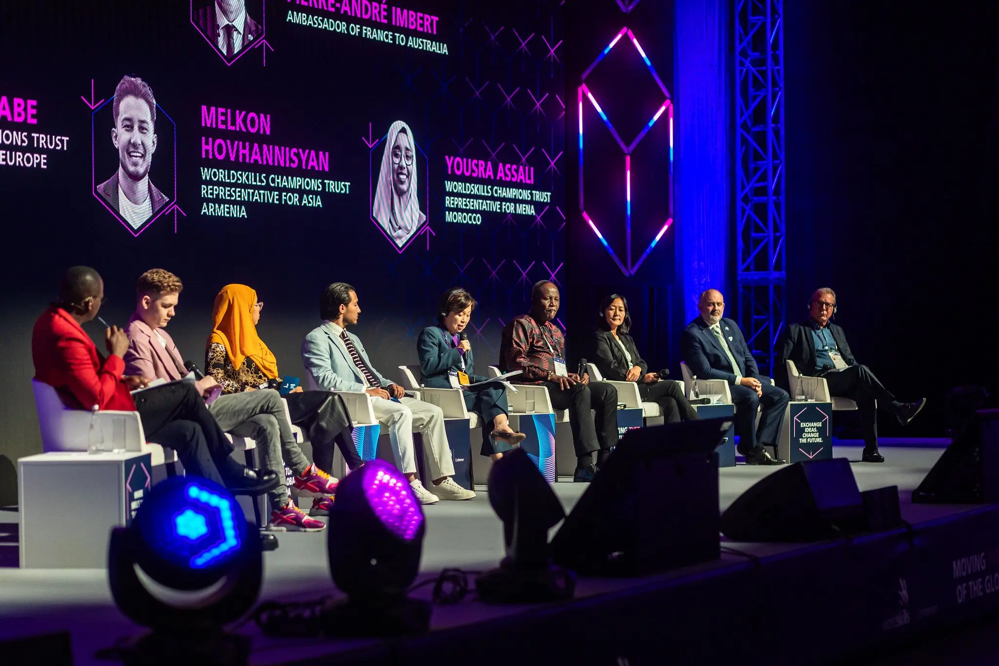 Melkon Hovhannisyan on stage with the panel of speakers at the WorldSkills Conference 2024 TVET policy session, with the speaker lineup displayed on the screen behind them